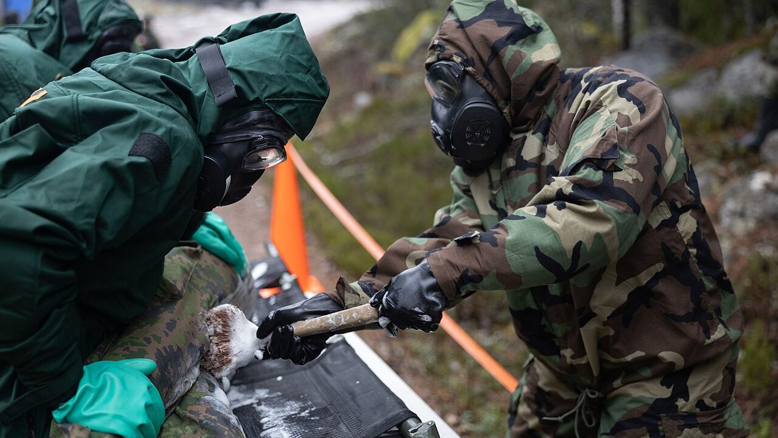 Two people in protective suits and respirators taking a sample during a CBRN exercise